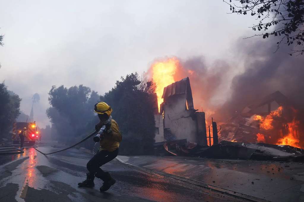 A firefighter battles the advancing Palisades Fire as it burns a structure in the Pacific Palisades neighborhood of Los Angeles, Tuesday, Jan. 7, 2025.